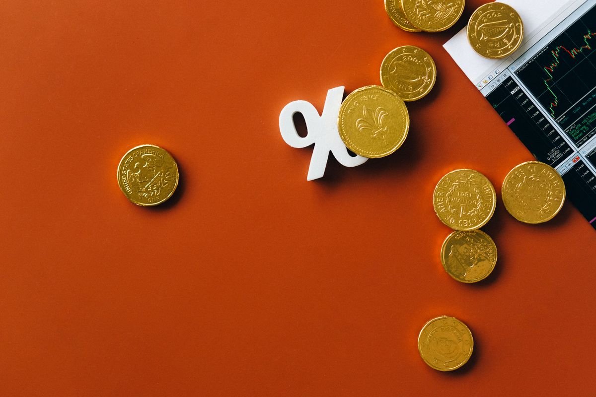 Coins beside a stock-market graph and a percentage symbol, representing interest rates.