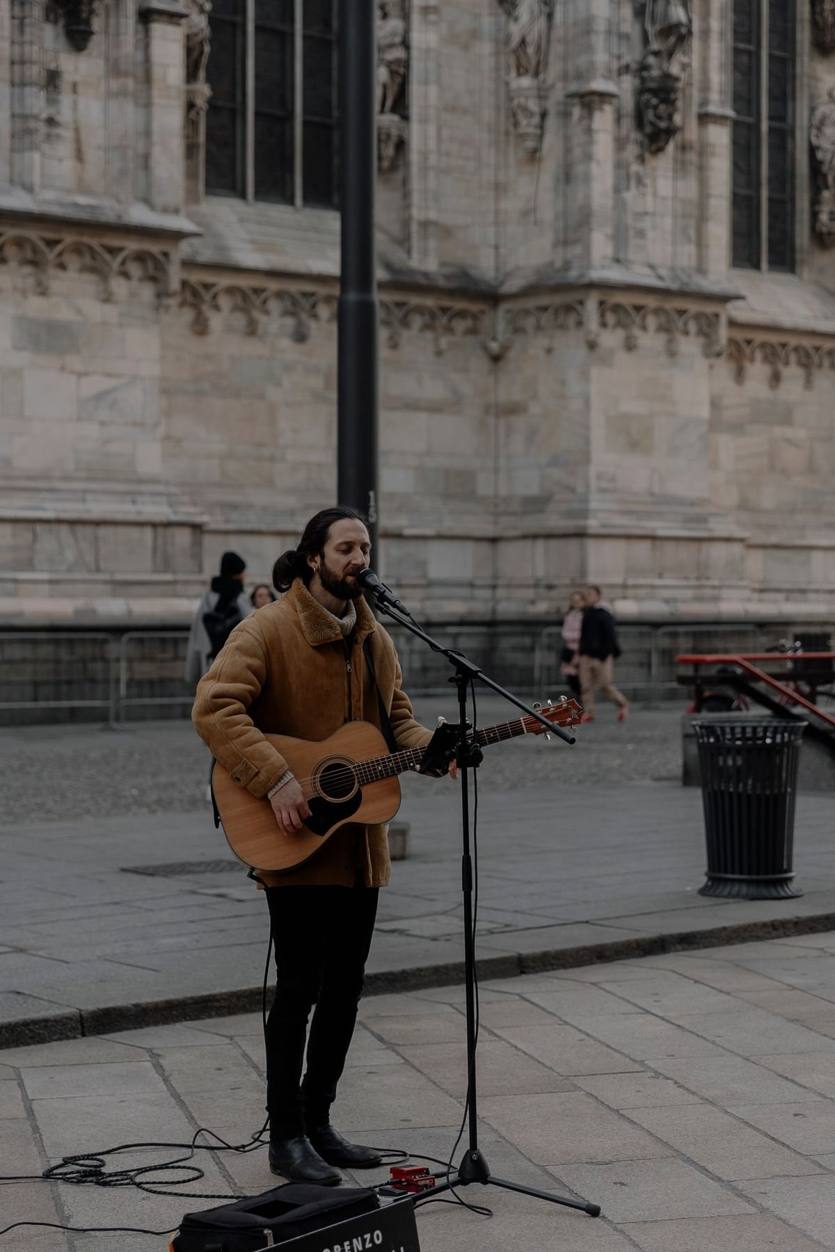 A street musician sings and plays acoustic guitar outside a historic building.