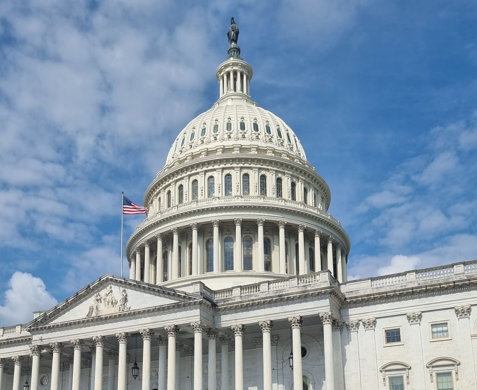 The US Capitol dome with an American flag against a blue sky in Washington, DC