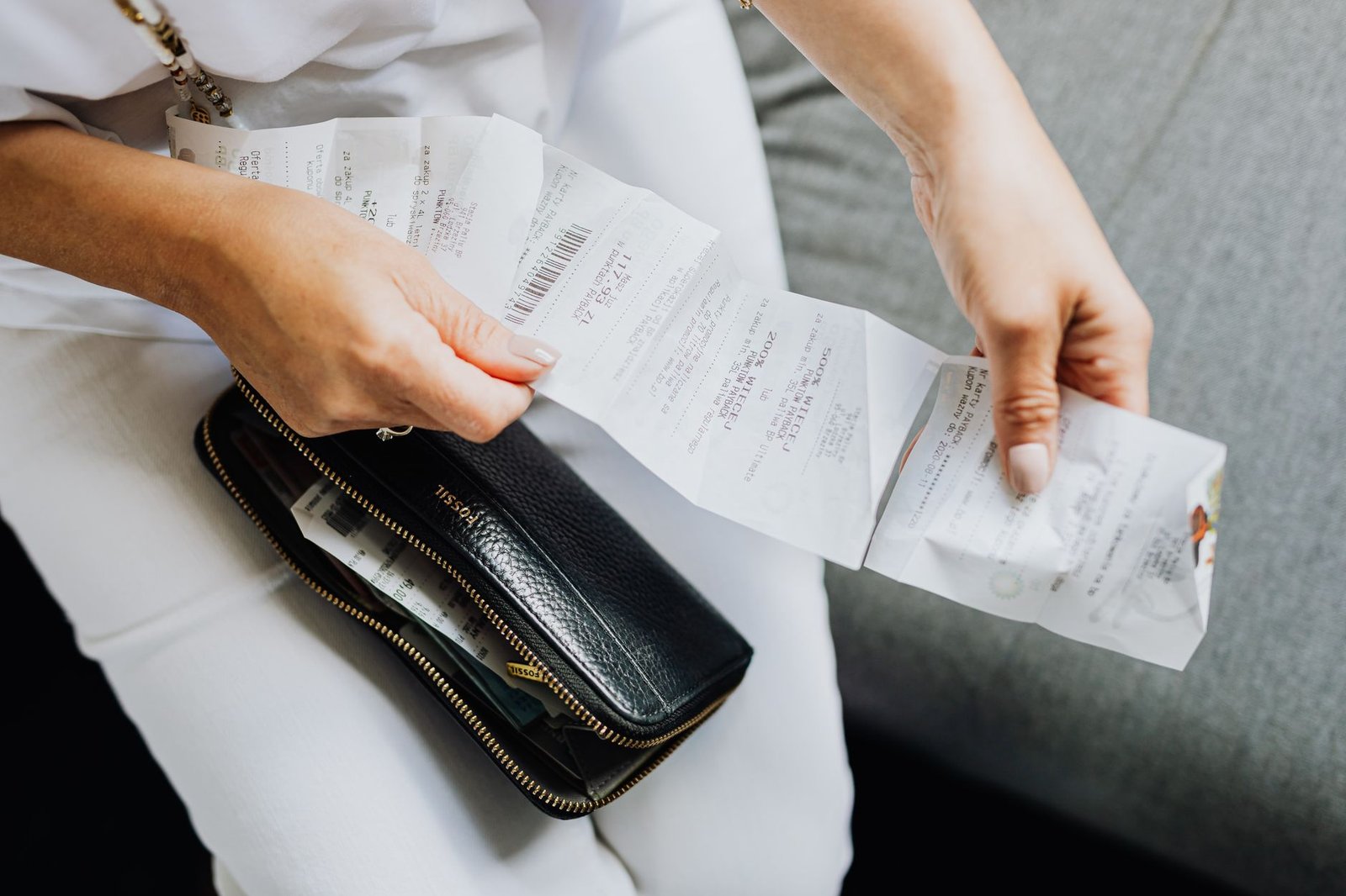 Hands sorting receipts and household bills spread across a table